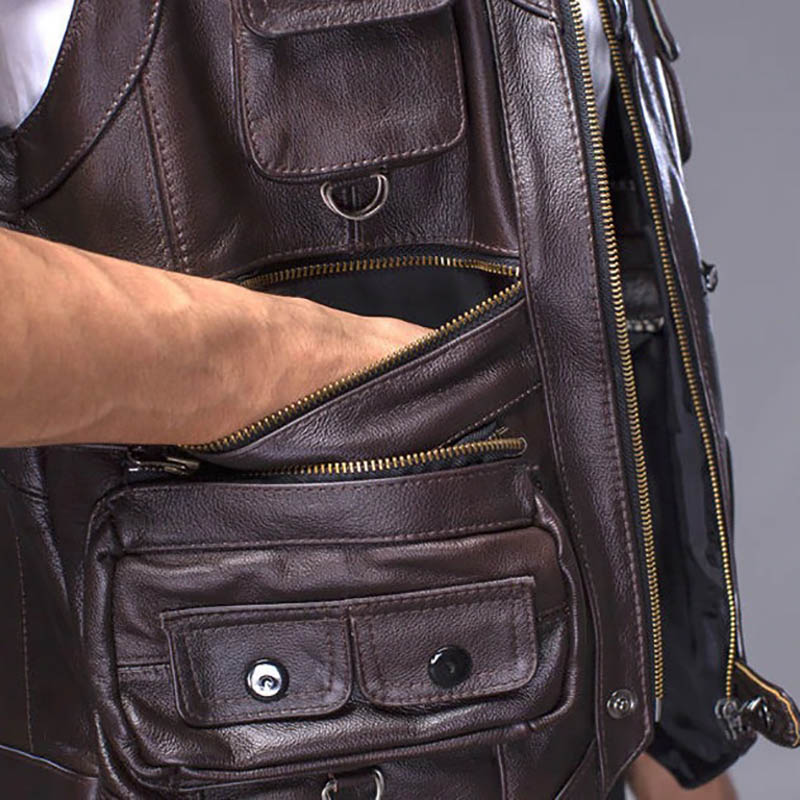 Close-up of a man's hand reaching into the pocket of a vintage brown leather biker vest, showcasing its stylish design.