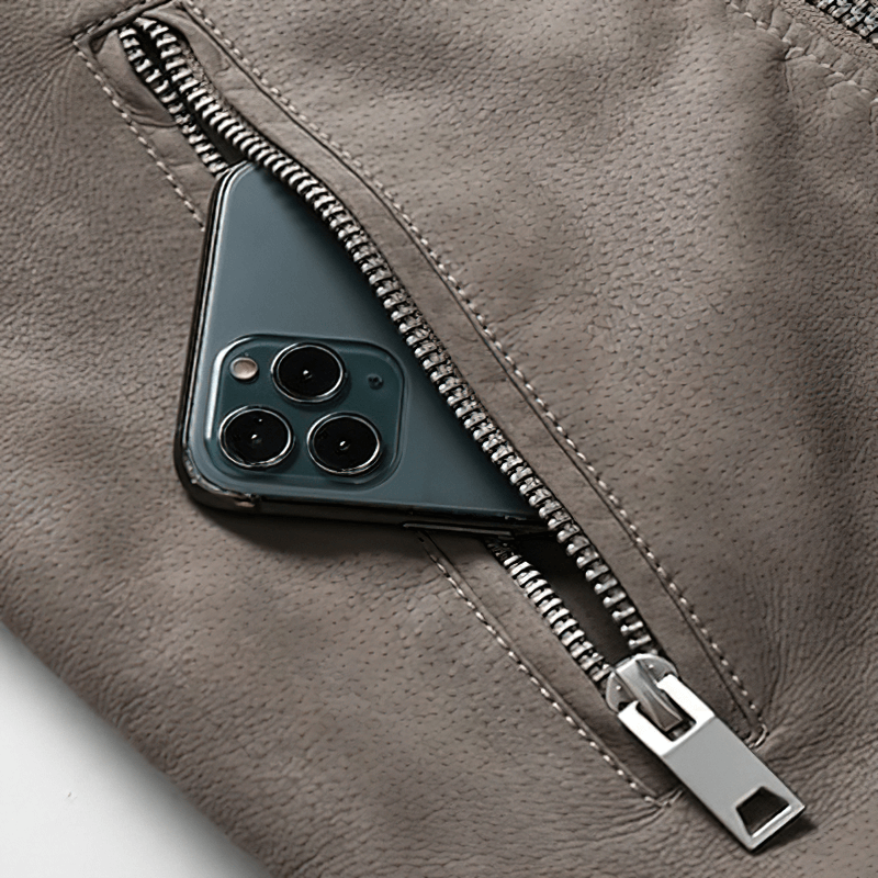 Close-up of a zipper on a vintage men's PU leather jacket revealing a smartphone inside.