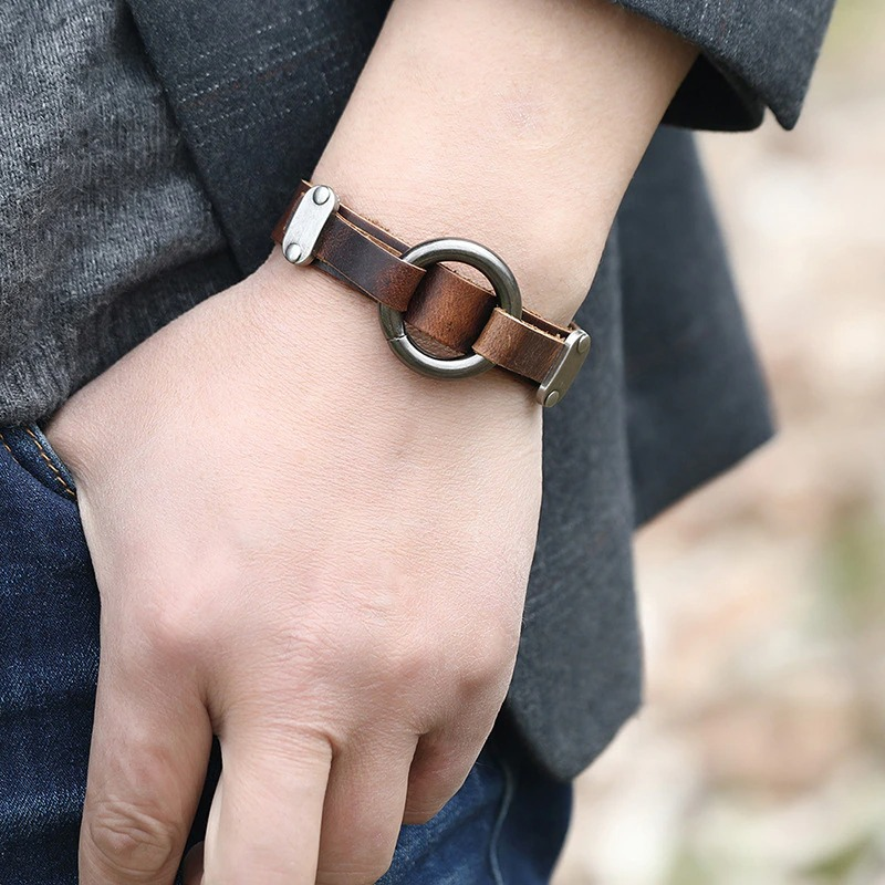 Hand wearing a vintage brown PU leather bracelet with alloy circle, showcasing punk style and unisex appeal.
