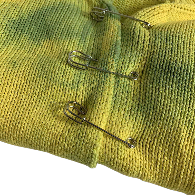 Close-up of a vintage green and yellow cropped cardigan with three silver safety pins.