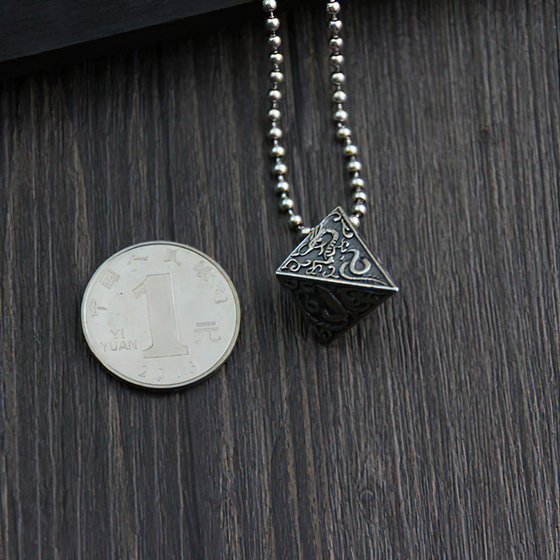 Vintage silver pendant in pyramid shape with animal designs, next to a 1 yuan coin for scale, on a wooden background.