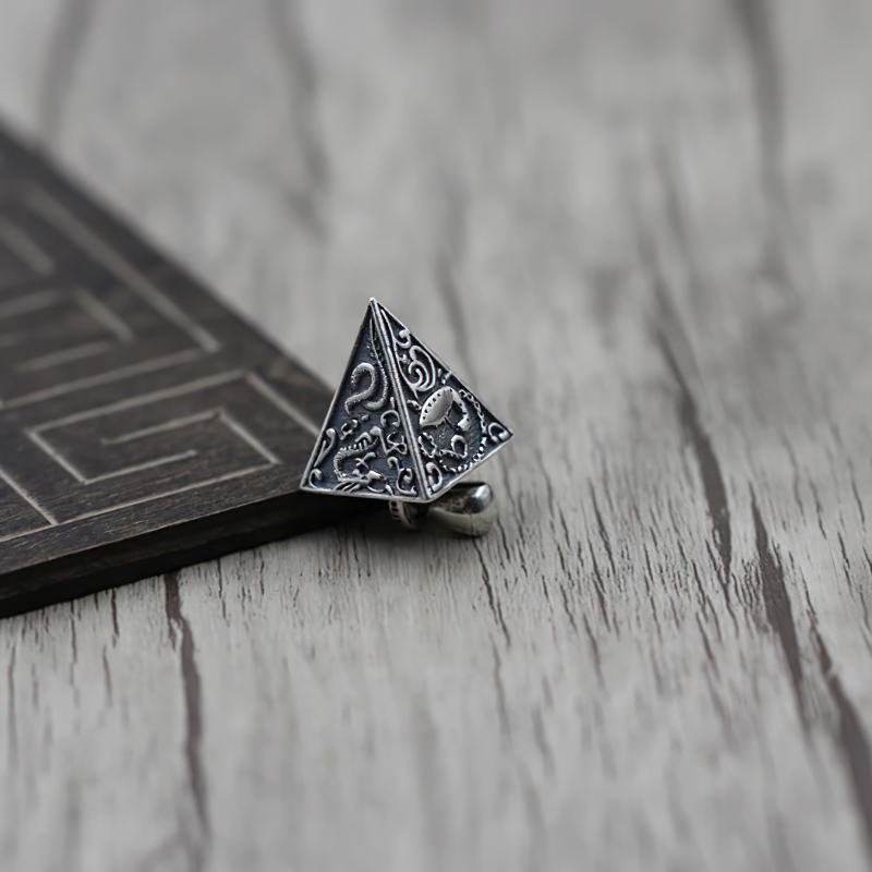 Vintage silver pyramid pendant with intricate animal designs on wood background.