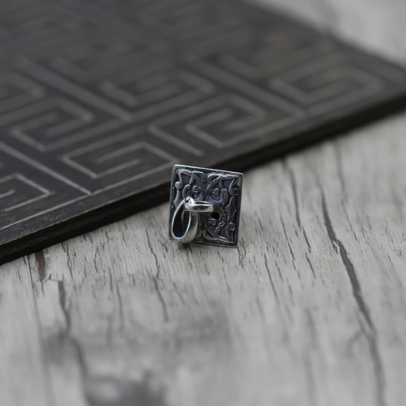 Vintage silver pendant with animal designs, pyramid shape on wood surface, perfect for unique jewelry lovers.