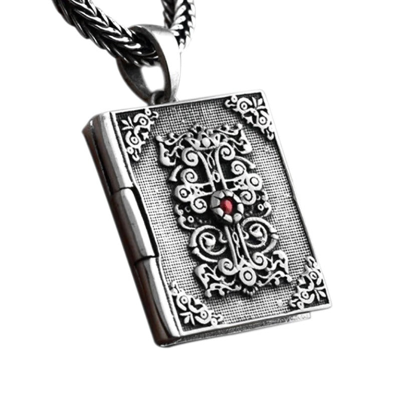Vintage silver religious pendant shaped like an ornate book, featuring intricate details and a red gemstone.