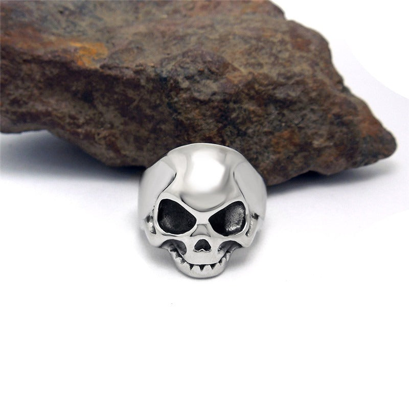 Vintage stainless steel skeleton skull ring on a rocky surface, perfect for alternative fashion and rock style jewelry.