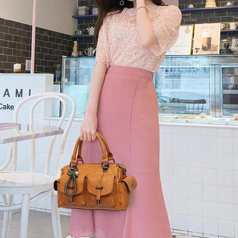 Stylish woman in pink skirt holding a vintage leather handbag with star pendant in a chic café setting.