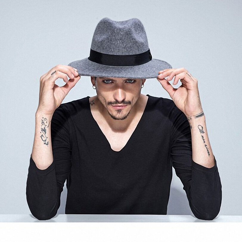 Stylish man wearing a wide brim grey wool fedora, showcasing alternative fashion with tattoos and a black shirt.