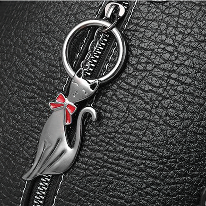 Close-up of a charming cat pendant with a red bow on a zipper pull for a vintage women's crossbody bag.