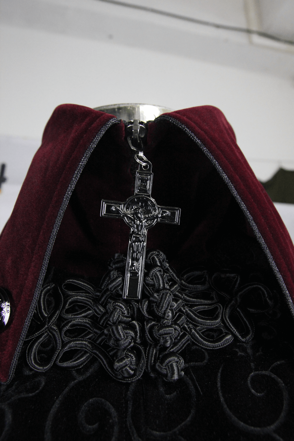 Close-up of gothic style coat with red collar and silver cross detail, showcasing intricate lace and embroidery.