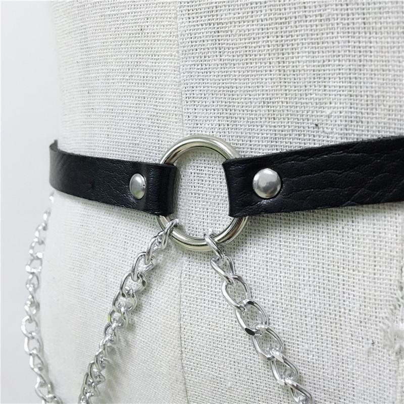 Close-up of a black faux leather body harness featuring metal chain links and a central ring, perfect for rock star fashion.