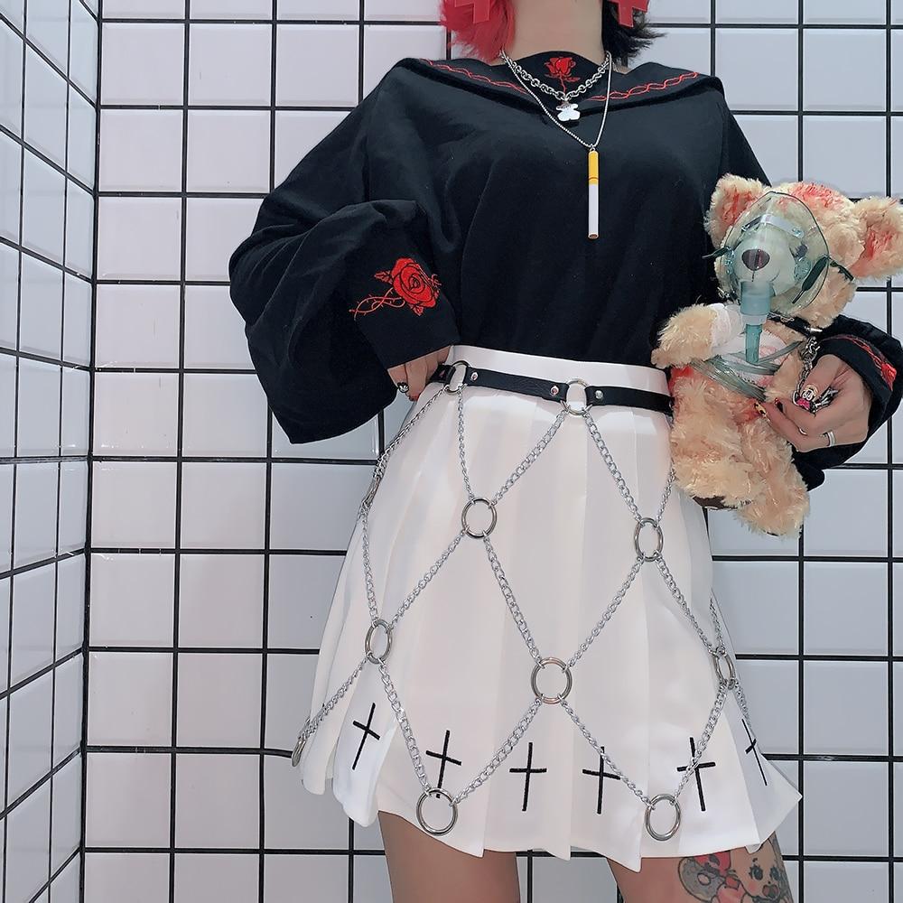 Women in a black top and white skirt adorned with a faux leather chain harness, showcasing rock star fashion style.