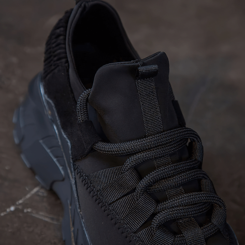 Close-up of stylish women's platform sneakers in black genuine leather, featuring unique lacing and textured details.