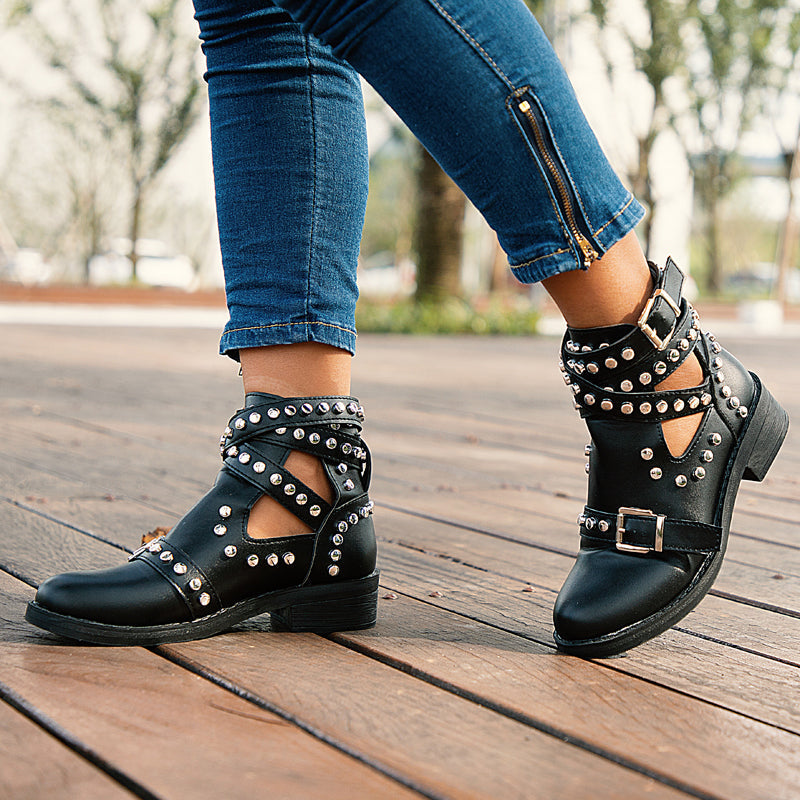 Stylish women's ankle boots with rivets and buckle straps, paired with fitted jeans on a wooden walkway.