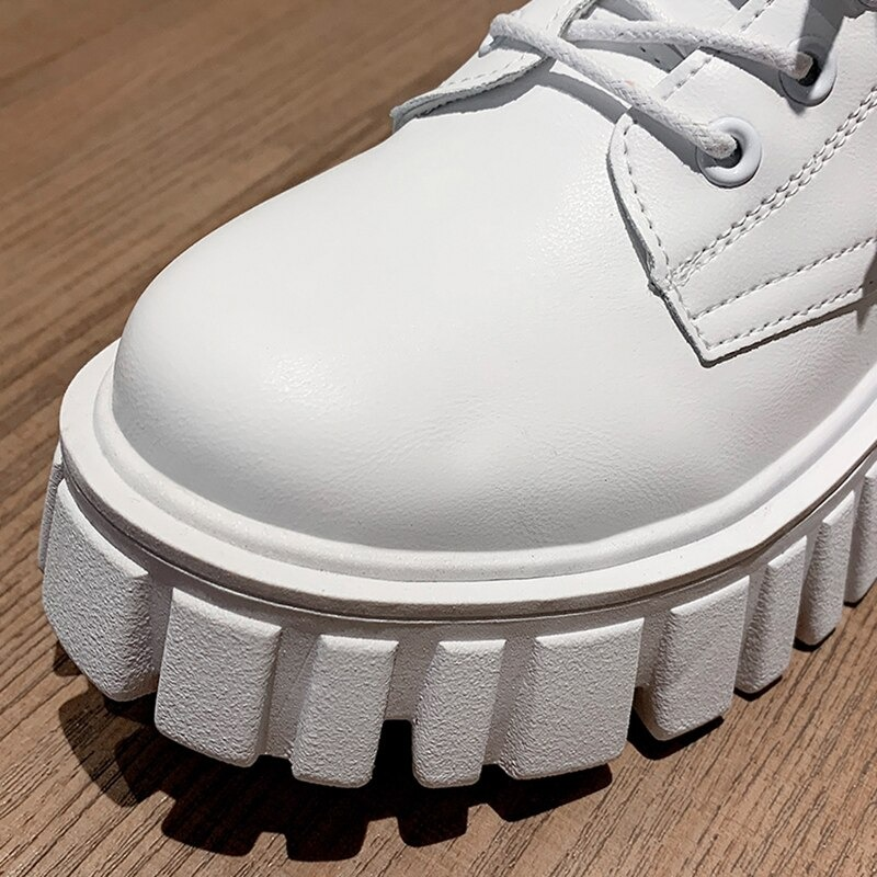 Close-up of women's white lace-up ankle boots with chunky platform sole on wooden surface.
