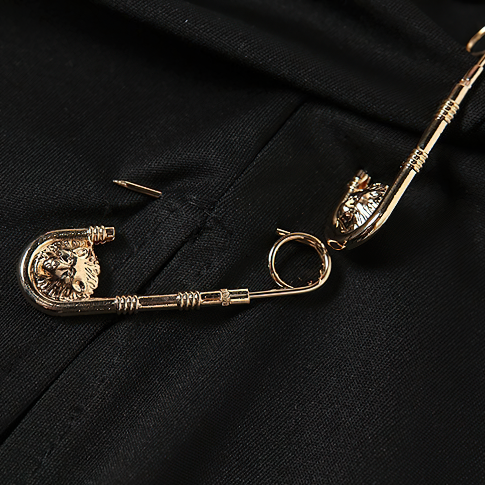 Close-up of gold lion-themed safety pins on a black fabric, perfect for gothic punk style outfits.