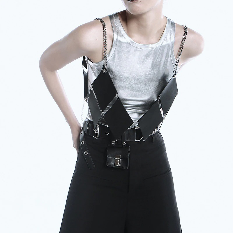 Stylish woman wearing a metallic silver tank top with a chic black harness and chain straps over black pants.
