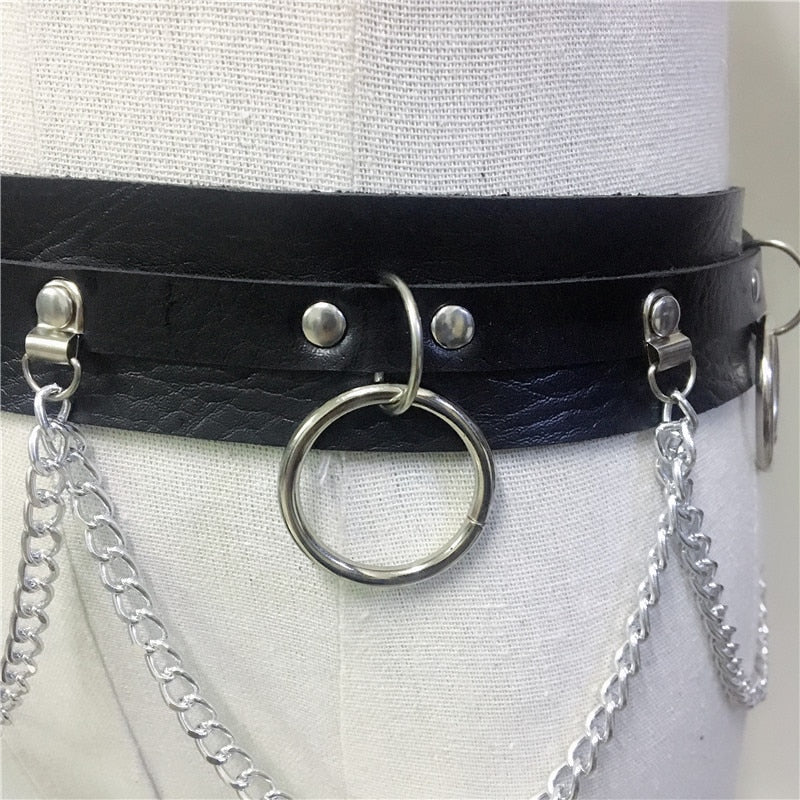 Close-up of a stylish black leather body harness with silver chains and metal rings for gothic fashion.