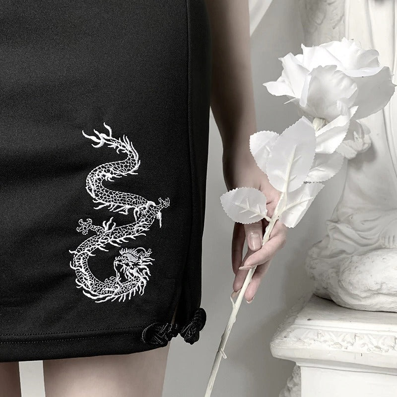 Close-up of a black bodycon mini dress featuring a white dragon print, elegantly held by a model with a flower.