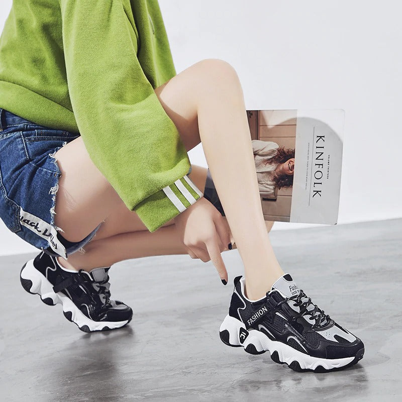 Women's chunky sneakers in black, stylishly paired with denim shorts and a green sweater.