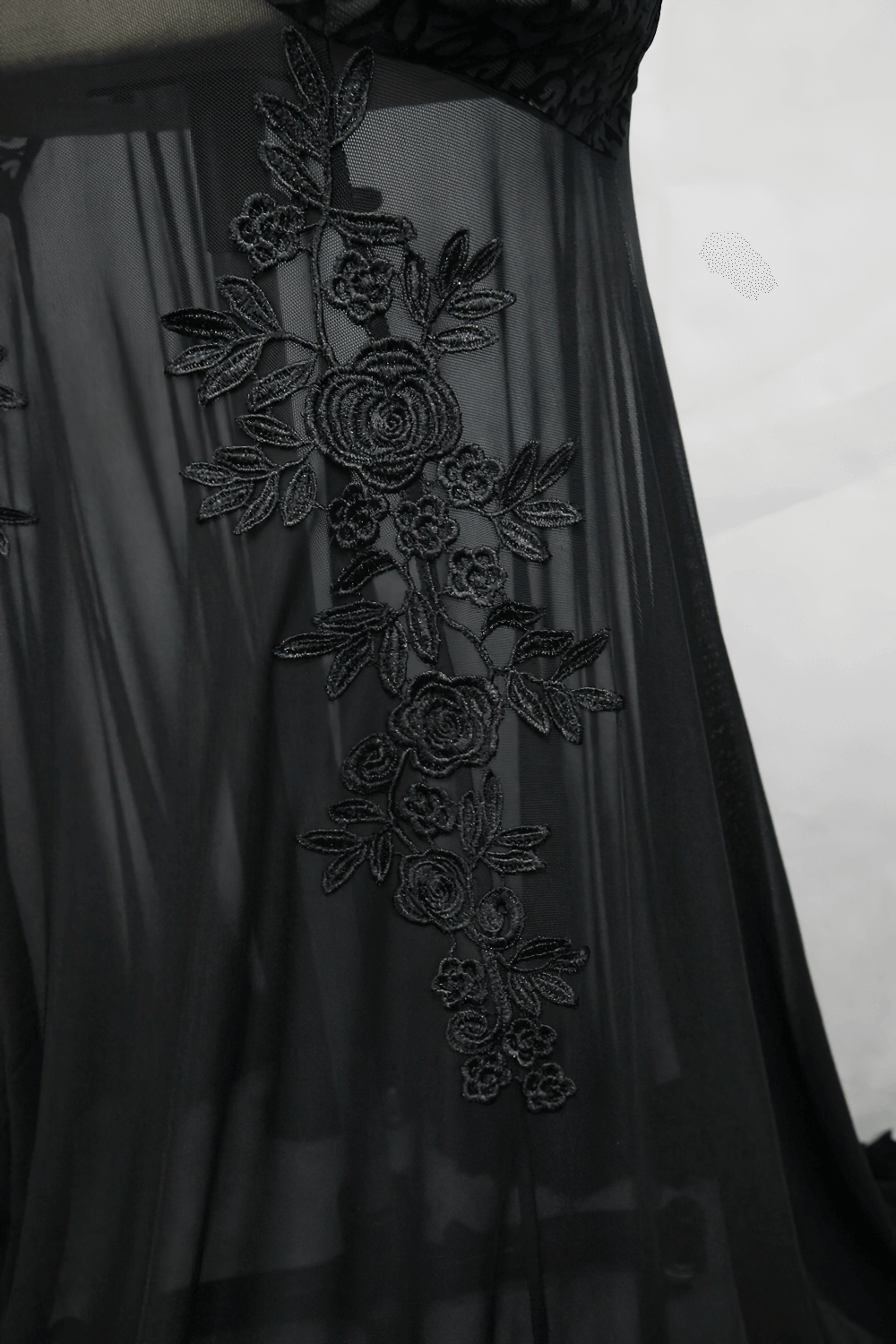 Close-up of black gothic long dress with transparent bottom and elegant floral embroidery details.