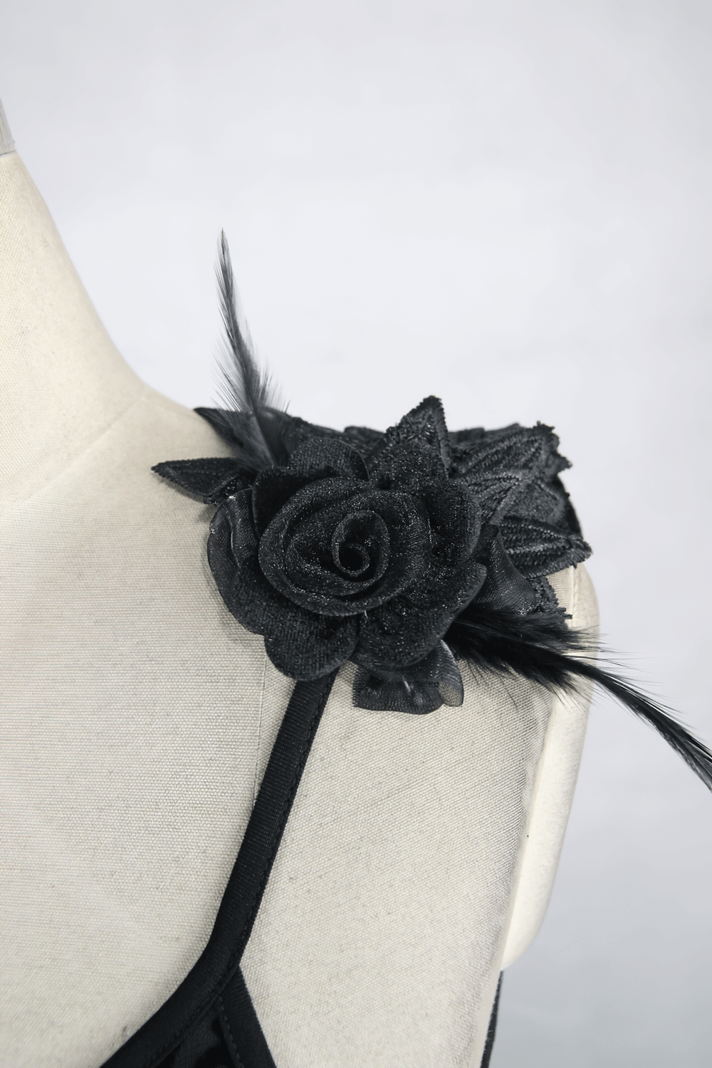 Close-up of a black floral embellishment on a gothic dress, featuring a rose and elegant feathers.