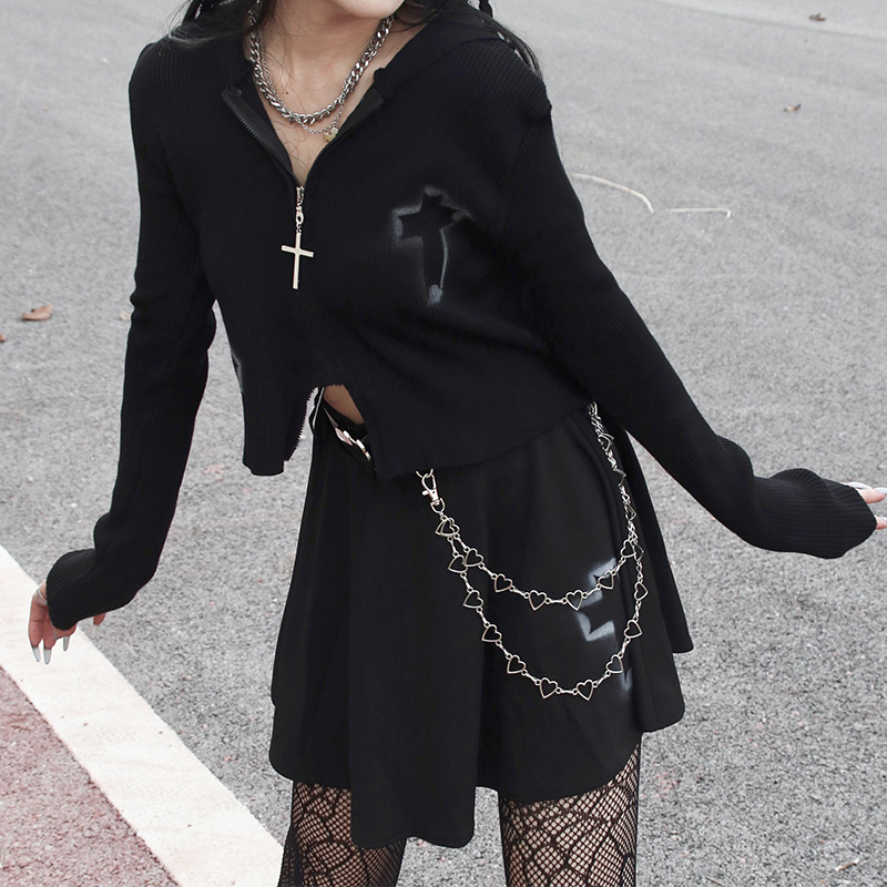 Stylish woman wearing a black zipper sweater with cross detail, paired with a casual skirt, on an urban background.