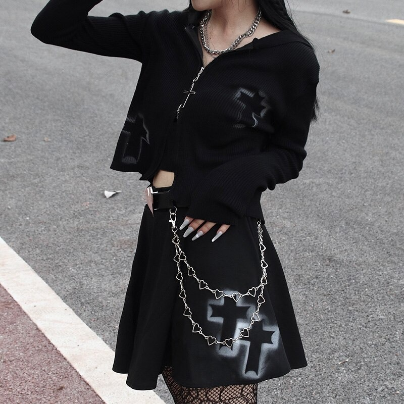 Stylish woman in a black gothic zipper sweater with cross design, paired with a flared black skirt and chain accessories.