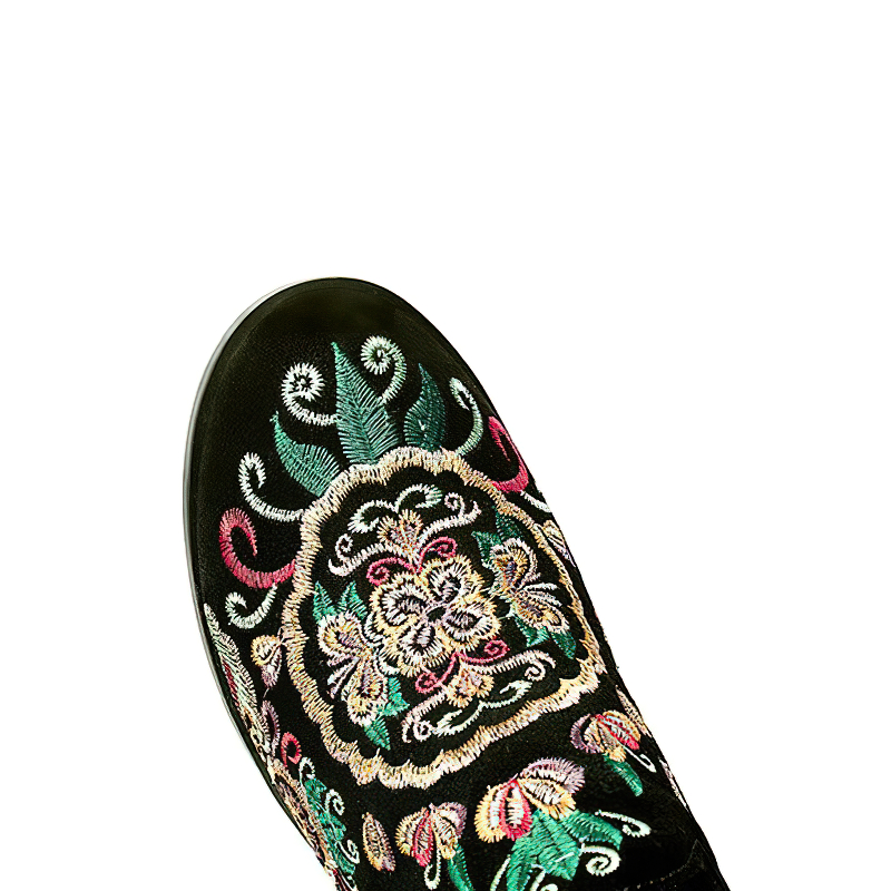 Close-up of embroidered pattern on women's knee-high black leather boot with colorful floral design.