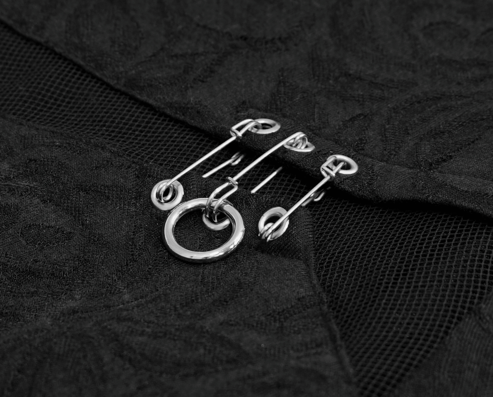 Close-up of silver safety pins and a ring accent against black fabric for gothic women's longsleeve top.