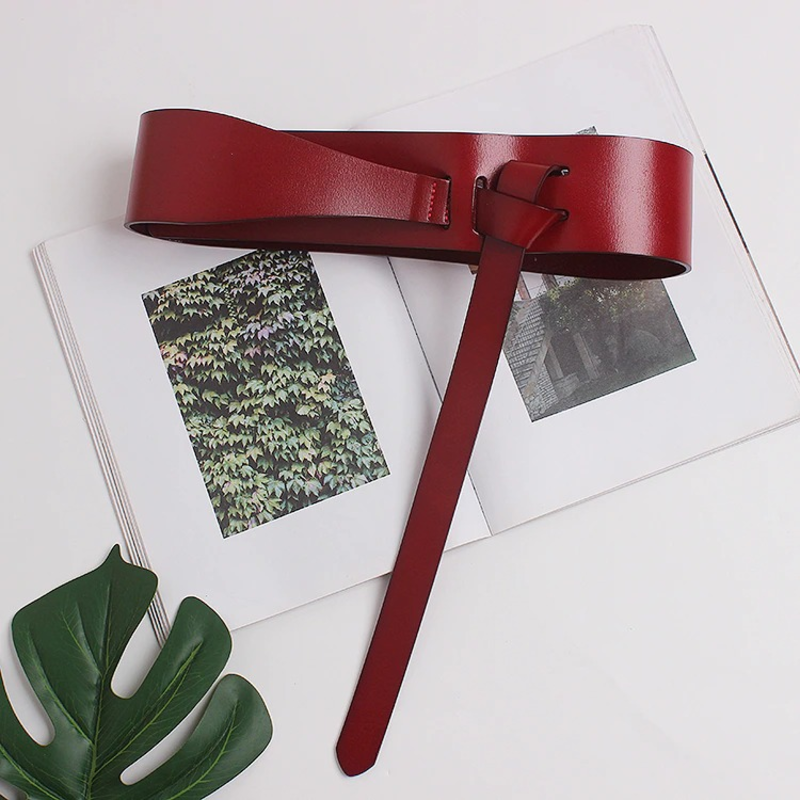 Stylish red wide PU leather belt resting on an open magazine, perfect for adding flair to any outfit.