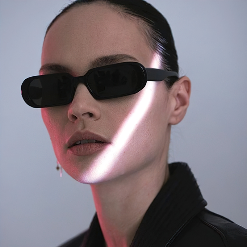 Female model wearing black luxury small oval sunglasses with dramatic lighting effect.