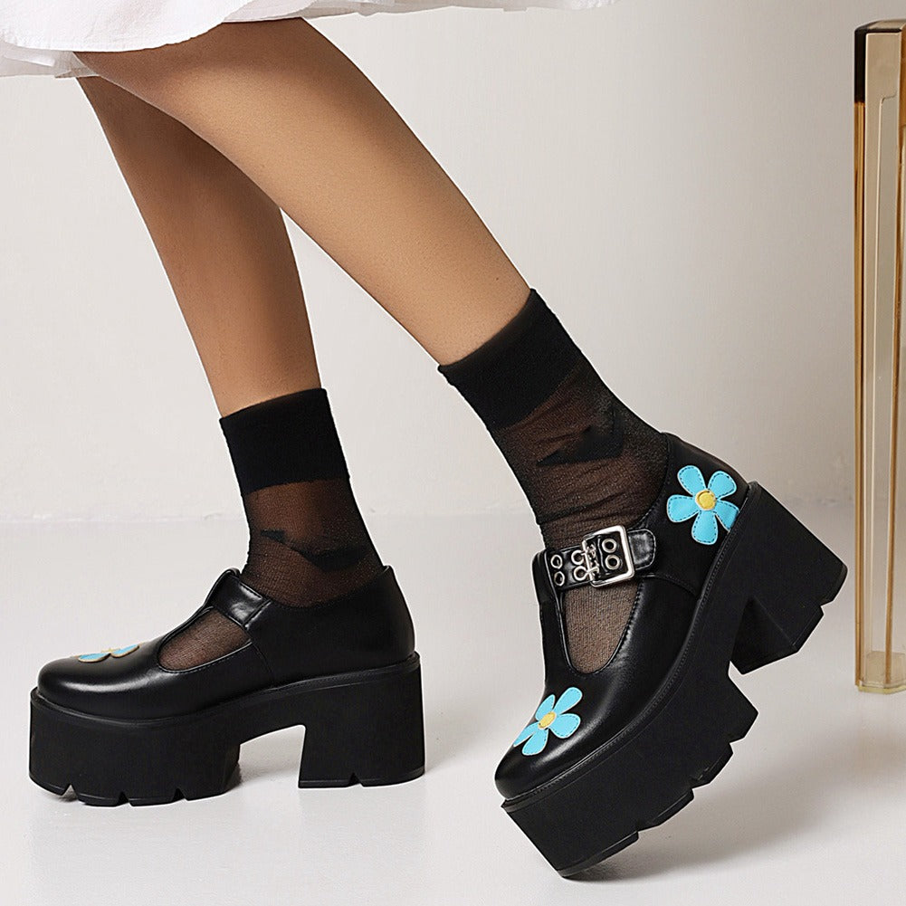 Women's punk style black platform pumps with blue flower design, paired with stylish black socks and a chic outfit.
