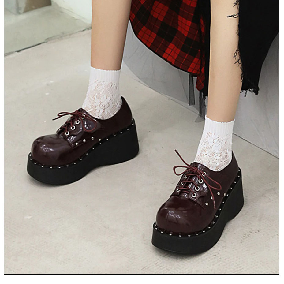 Trendy women's punk style platform shoes in dark burgundy with lacing, paired with lace socks on a stylish outfit.