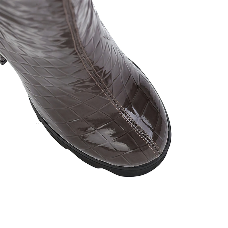Close-up of stylish women's patent leather high heel boots with a quilted design and silver chain accents.