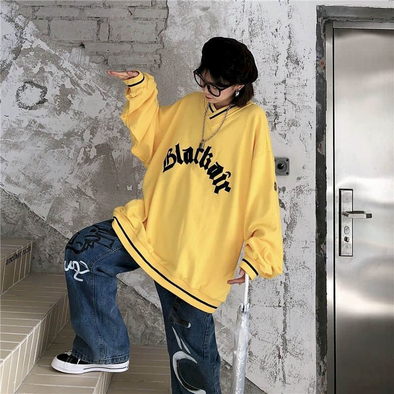 Model wearing a stylish oversized yellow sweatshirt with 'Blackair' lettering, paired with baggy jeans.