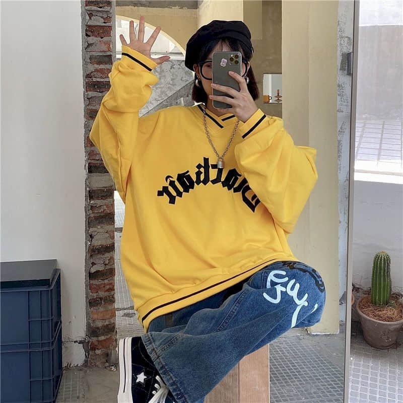 Fashionable woman in yellow oversized sweatshirt posing casually, showcasing trendy letter patch style.