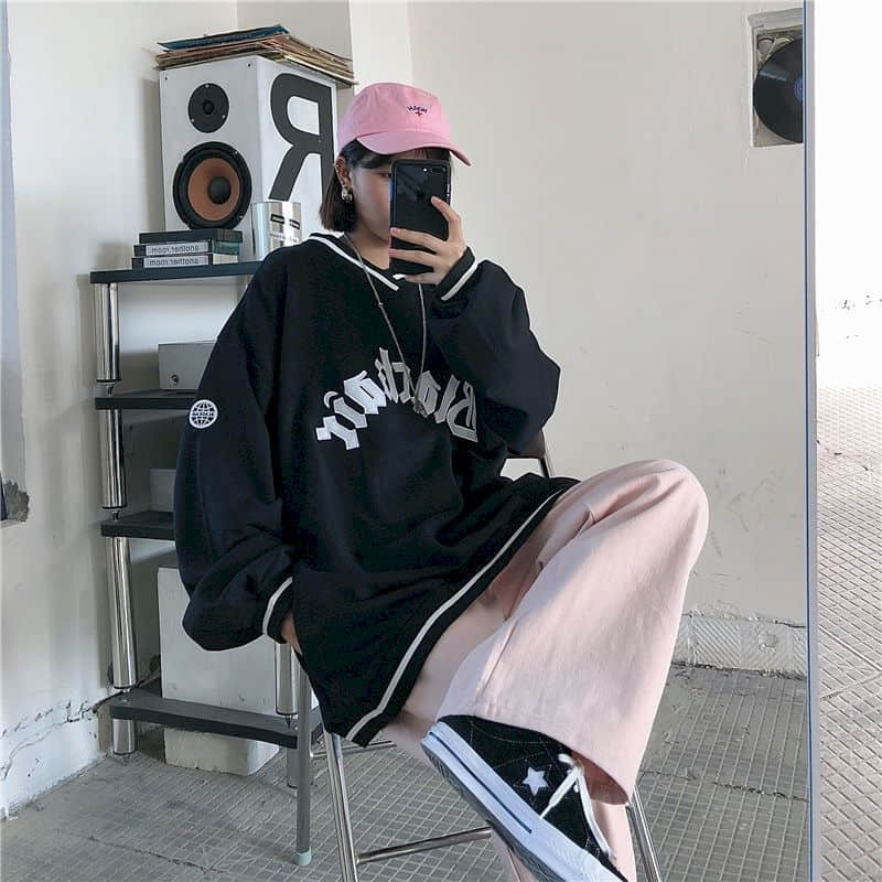 Casual woman wearing an oversized black V-neck sweatshirt and pink cap, showcasing trendy streetwear style.